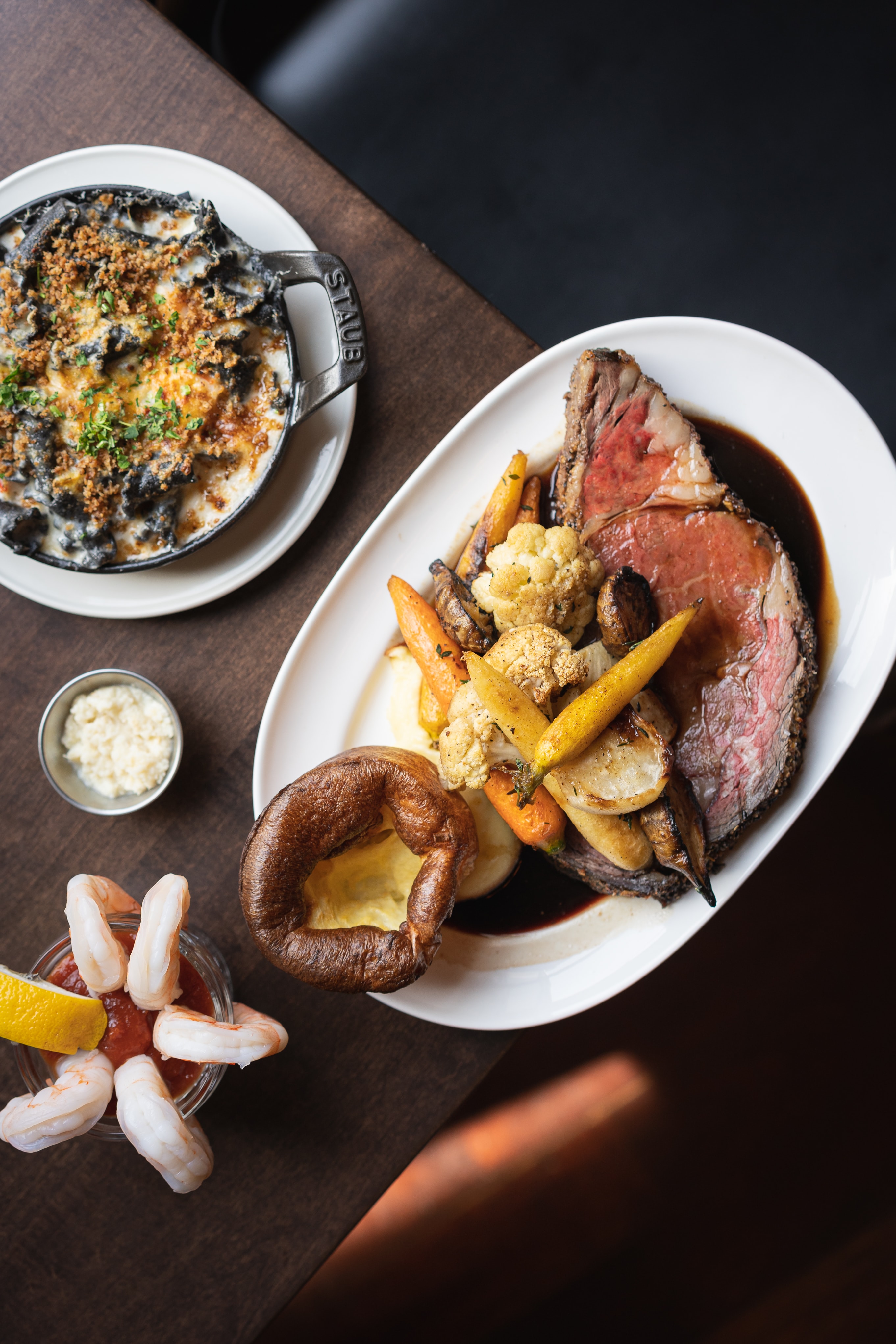 Angled overhead of Sunday Roast with prime rib, Yorkshire pudding, Staub mac and cheese, and shrimp cocktail at The Berczy Tavern in Toronto